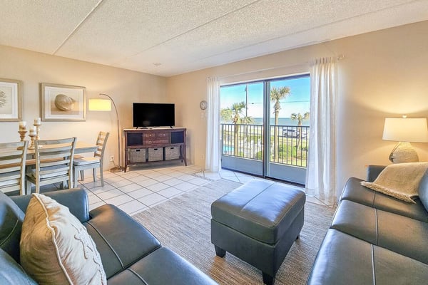 Beachfront condo living room with ocean and palm tree views, leather seating, TV, and glass balcony doors
