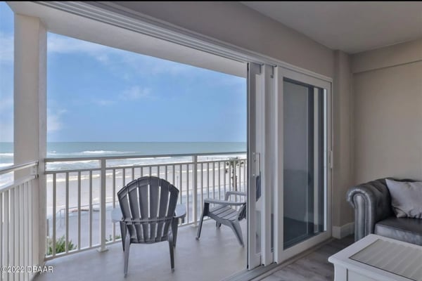 Oceanfront balcony with two chairs, white railing, and sliding glass doors opening to beachfront view